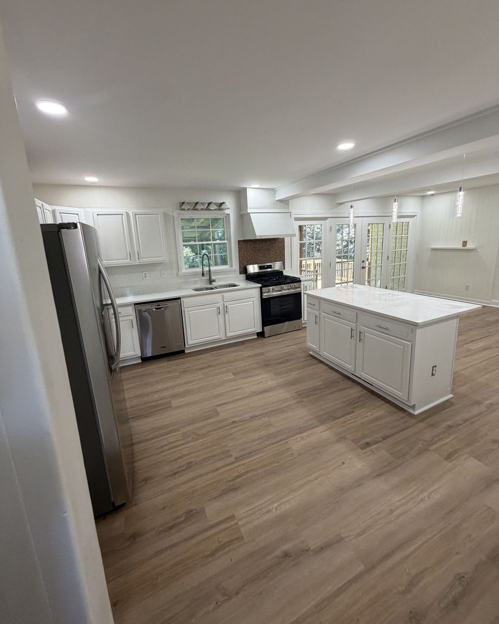 Renovated kitchen with white cabinets, a white island, stainless appliances, and wood-look flooring