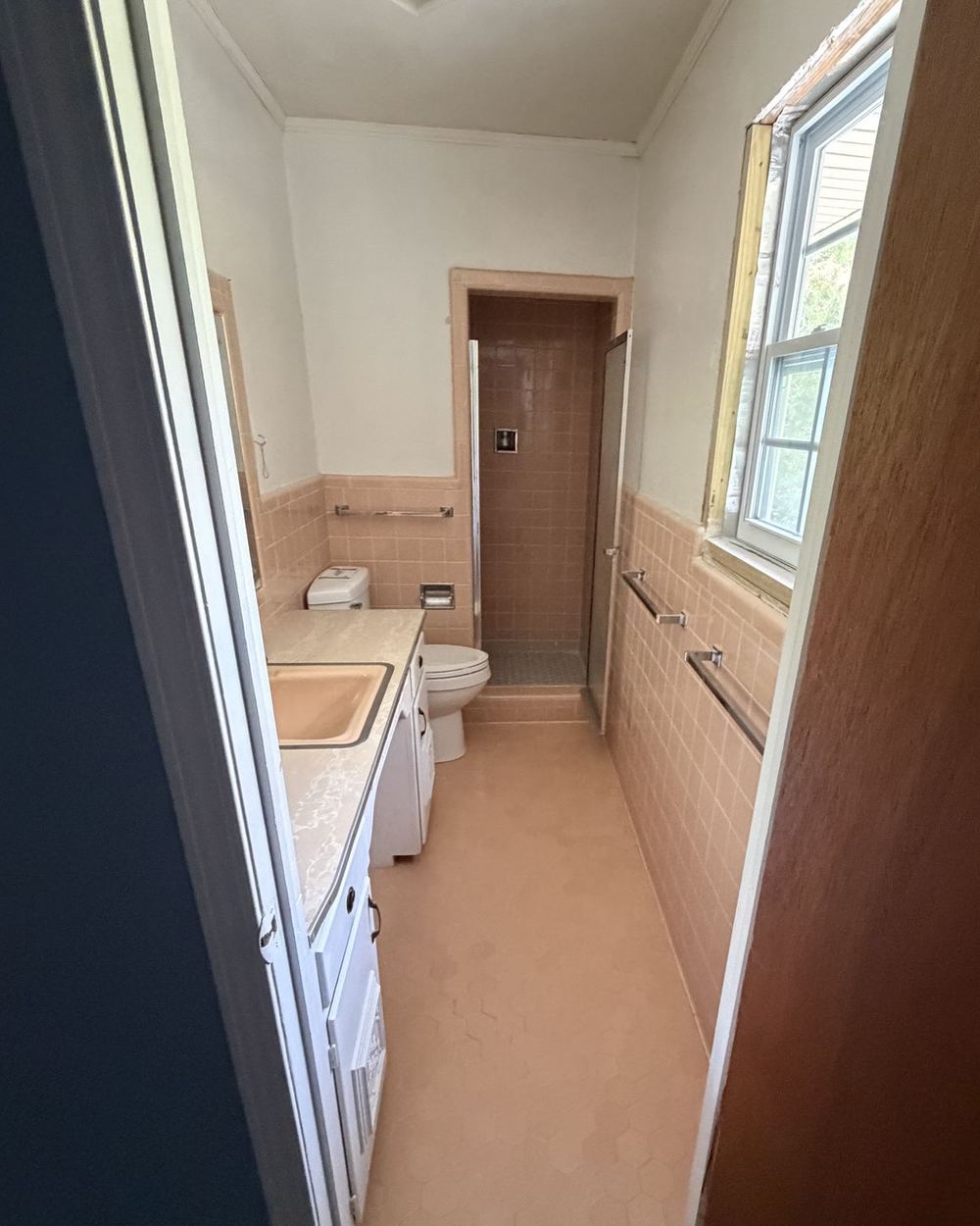 Hall bathroom before renovation: pink wall tile, an old vanity, and a narrow doorway