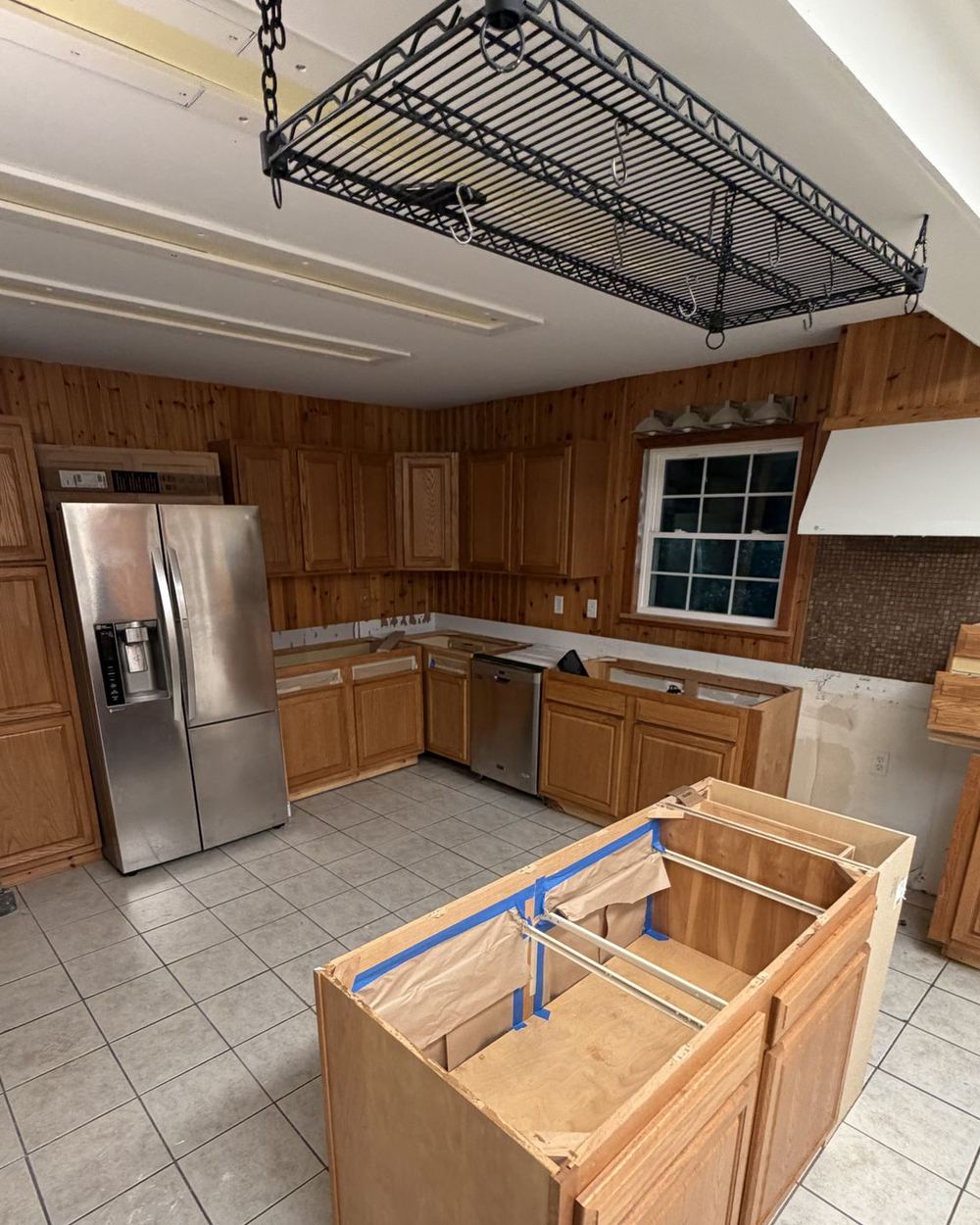 Kitchen before renovation: wood cabinets and paneling, tile floor, and an unfinished island