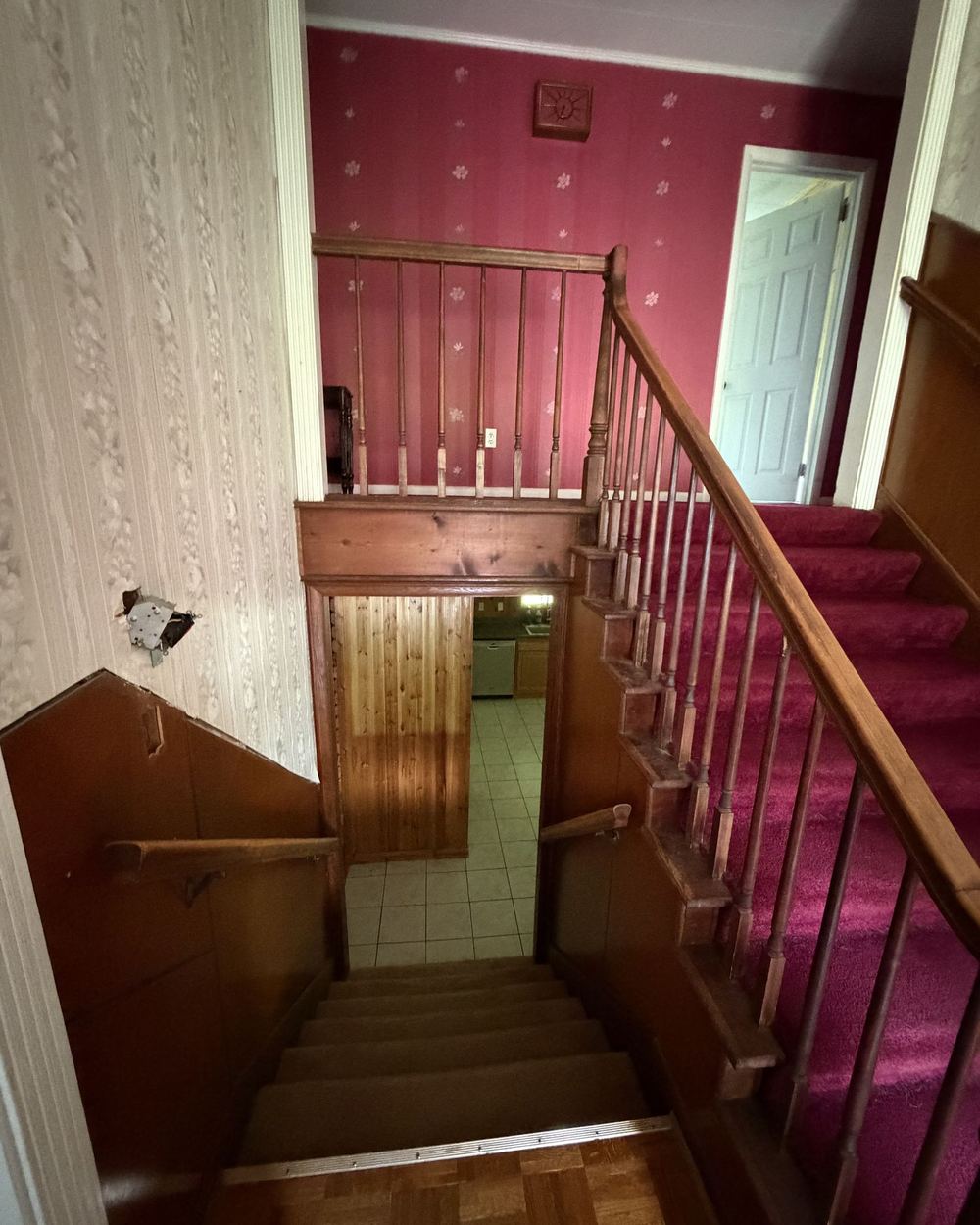 Foyer staircase before renovation: red carpet, red wallpaper, and dark wood paneling