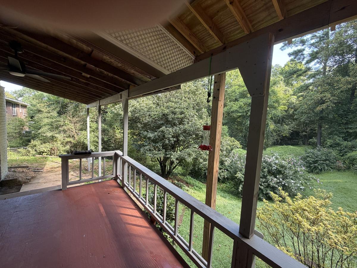 Covered back porch with a wood ceiling, railings, and a wooded backyard view