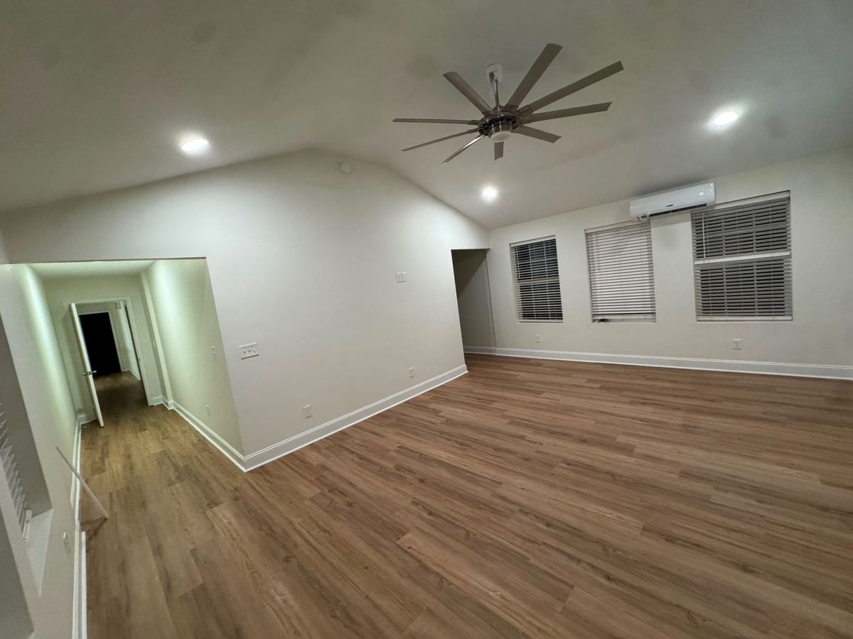 Bright living room with a vaulted ceiling, ceiling fan, and wood-look floors