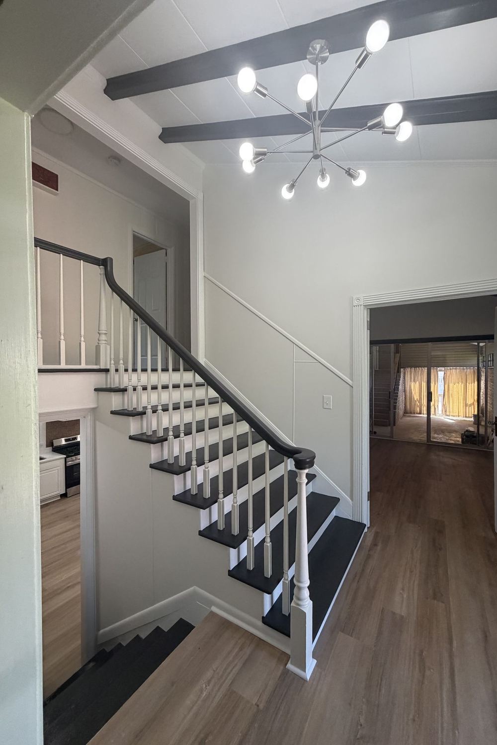 Renovated staircase with black and white treads, white railings, and a modern chandelier